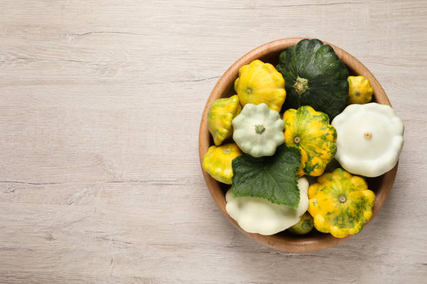 fresh ripe pattypan squashes in bowl on light wooden table, top view. space for text - pattypan squash imagens e fotografias de stock
