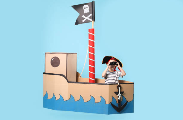 istock Little boy playing with binoculars in pirate cardboard ship on turquoise background 1393170531