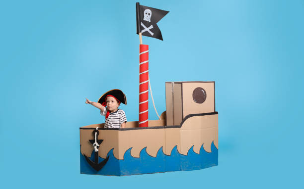 istock Cute little boy playing in pirate cardboard ship on turquoise background 1393170644