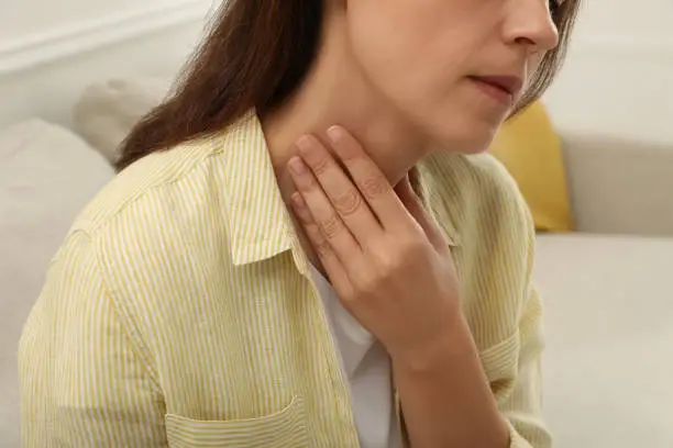 Mature woman doing thyroid self examination indoors, closeup