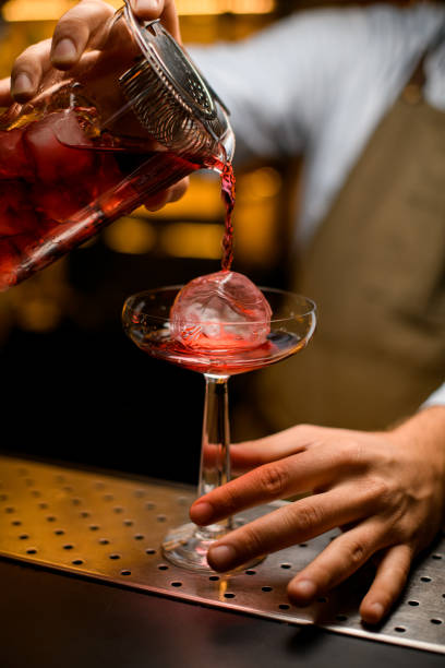 istock bright cocktail poured into a glass with ice from a mixing cup filtered through a strainer 1393171565