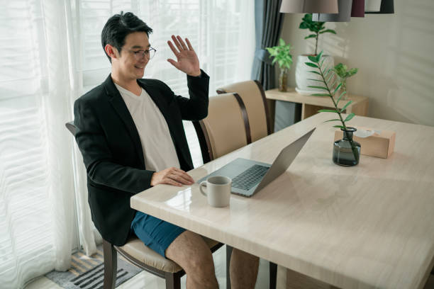 istock Man wearing a suit on top and pants boxers on bottom Having  video conference using laptop waving his hand to say hello in the living room at home. Working from home. 1393171611