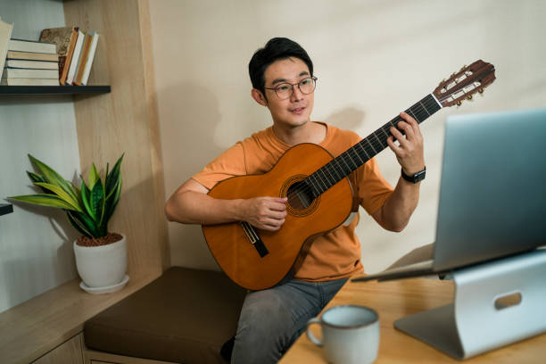 istock Smiling Asian man teaching Acoustic guitar  through a video call at home. 1393171614
