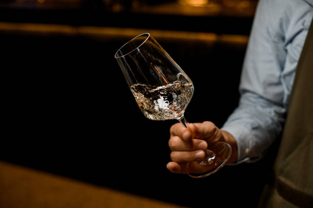 hand of man gently holds tilted transparent wine glass with a drink - transparent holding glass focus on foreground imagens e fotografias de stock