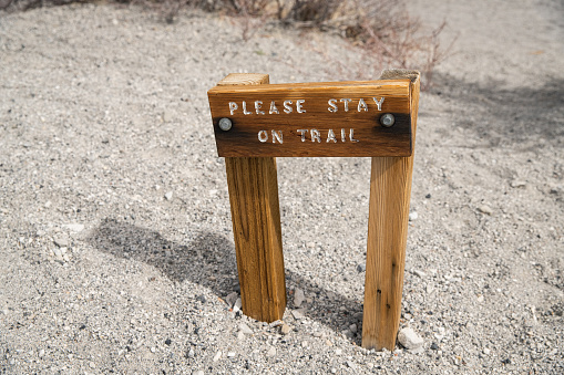 Wooden sign at trailhead in the desert informing hikers to stay on trail to lessen their  environmental impact