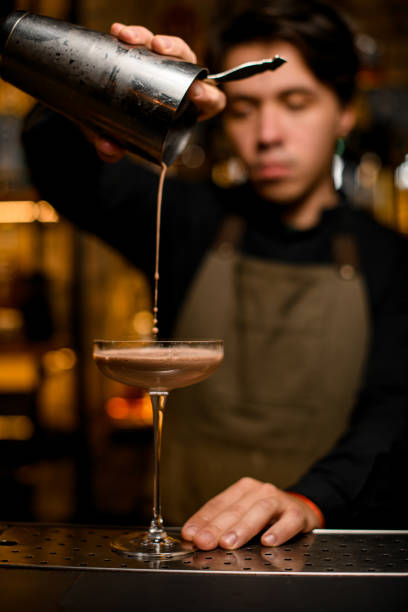 istock Young bartender professionally pours brown cocktail from shaker into glass 1393177471
