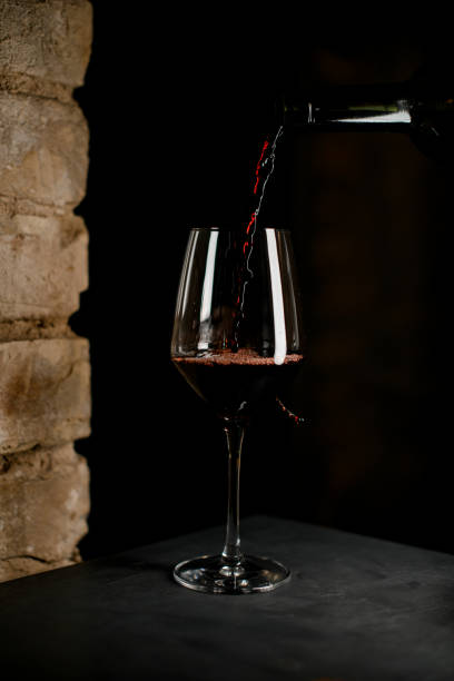 vue rapprochée de la bouteille sombre jusqu’au verre à vin à moitié cristallin avec du vin rouge - wineglass glass crystal studio shot photos et images de collection