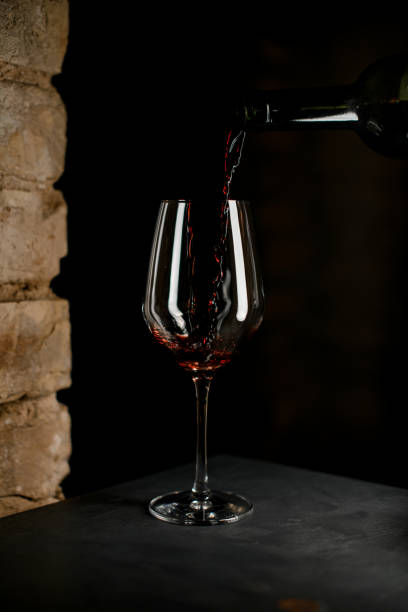 vue rapprochée d’une bouteille sombre remplissant un verre à vin cristallin avec du vin rouge - wineglass glass crystal studio shot photos et images de collection