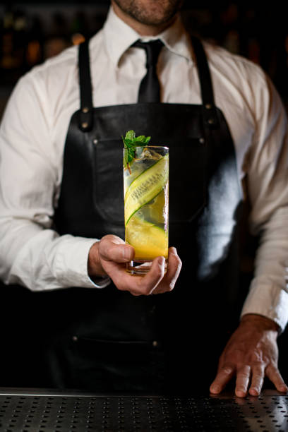 glass of cocktail with cucumber slices decorated with fresh mint in male hand - transparent holding glass focus on foreground imagens e fotografias de stock