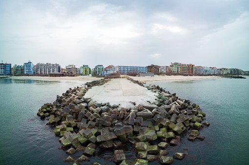 Panorama of a small wide stone pier - a breakwater near a wild empty sandy beach in the raging blue undulating Black Sea, near a small Bulgarian resort town
