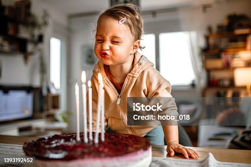 istock Little birthday girl blowing out candles on cake at home 1393192452