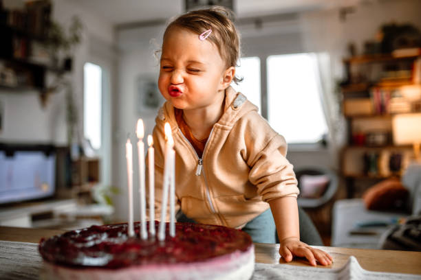 little birthday girl blowing out candles on cake at home - soprar imagens e fotografias de stock