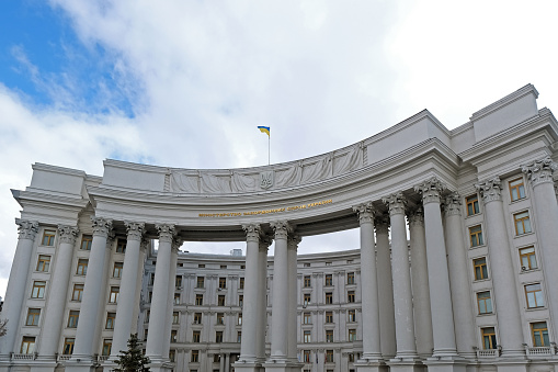 A building of Ministry of foreign Affairs of Ukraine. Marble white arch, with Ukrainian flag on top of it. Arch is supported on thin pillars. Clear and blue sky above the construction