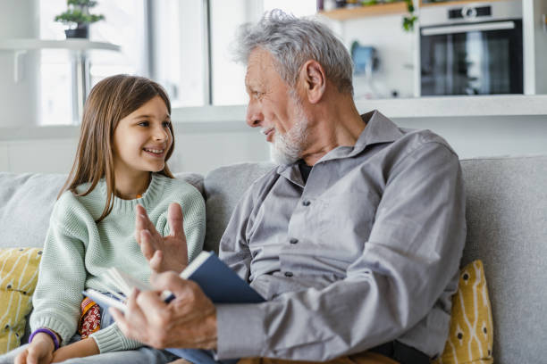 nonno che legge un libro alla nipote a casa - nipote femmina foto e immagini stock