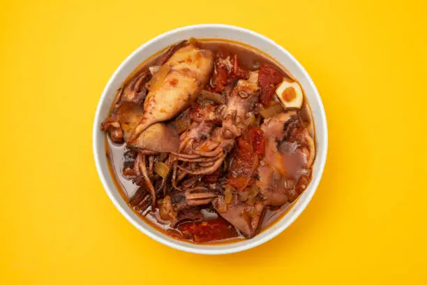 Photo of fresh tasty squid stew in white bowl on yellow