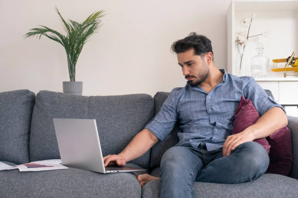 istock Young man sitting in his armchair at home and working on computer 1393201755