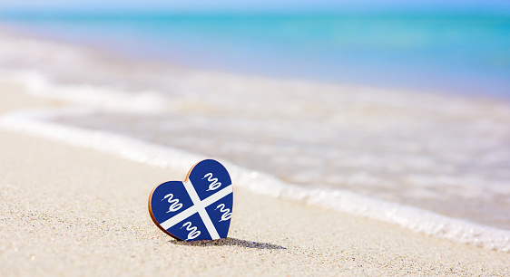 Flag of the Martinique in the shape of a heart on a sandy beach. The concept of the best vacation in Martinique resorts