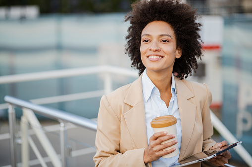 Young African American businesswoman holding digital tablet and reusable coffee cup