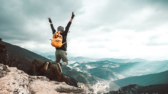 Man traveler on mountain summit enjoying nature view with hands raised over clouds - Sport, travel business and success, leadership and achievement concept