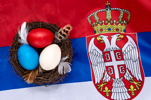 Multicolored decorated Easter eggs in a nest on the flag of Serbia. Easter concept.