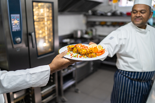 A chef handing a white plate of delicious low carb chicken, a side of tomatoes and lemon slices  to an unrecognisable person