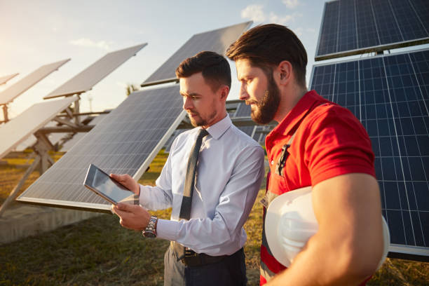 fokussierter männlicher vorgesetzter, der tablet mit techniker in der nähe von sonnenkollektoren teilt - solar panel fotos stock-fotos und bilder