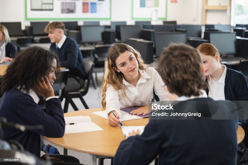 Adolescent students interacting in round-table discussion Multiracial group of classmates in school uniforms sitting together, working collaboratively, debating and taking notes about educational subjects. UK Stock Photo