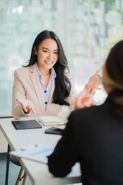 A meeting of two young Asian businesswomen to collaborate and work as a team for success in business and finance. Affiliate greetings and ideas with documents, graphs and a tablet on the table. stock photo