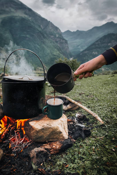 Dark big pot or cauldron, cooking pan with boiling water inside above the fire somewhere in the park or mountains, camping concept