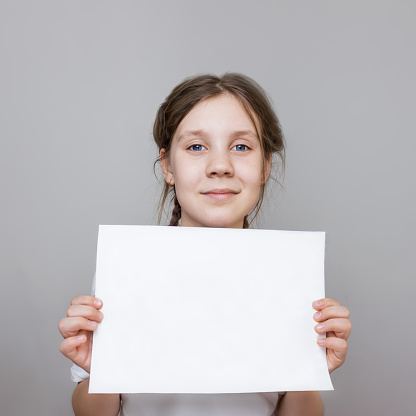 child girl in a white t-shirt holding awhite paper,  mockup,portrait of a teenage girl with blue eyes, selective focus