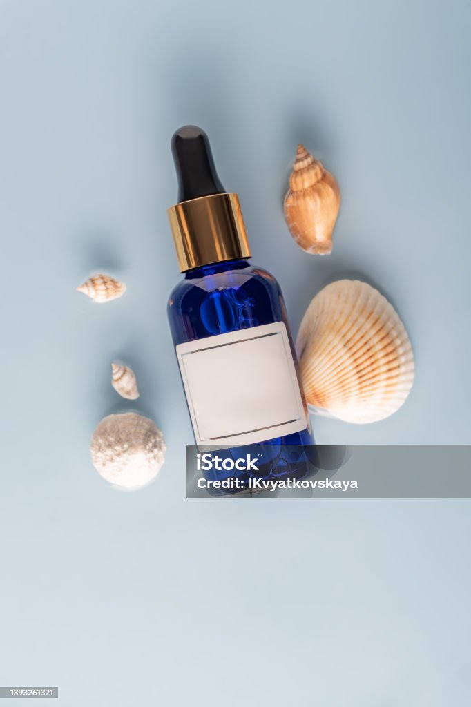 moisturizing face serum on a blue sea background with seashells.The concept of cosmetics with marine extracts. mockap label for your design moisturizing face serum on a blue sea background with seashells.The concept of cosmetics with marine extracts. mockap label for your design. Ampoule Stock Photo