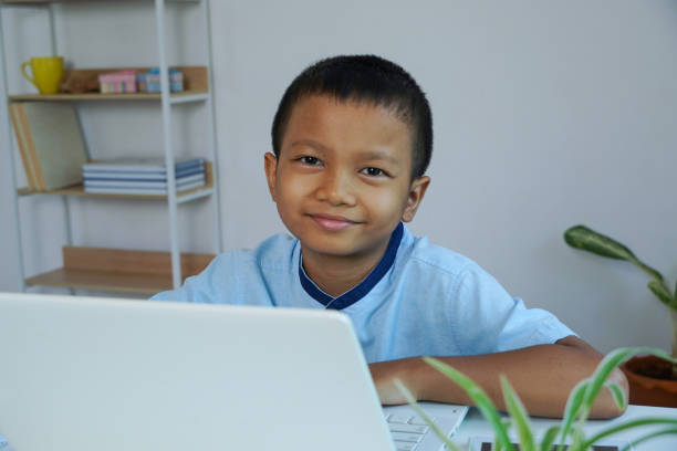 istock Asian boy smiling and looking a camera. using laptop for self learning at home. 1393261349