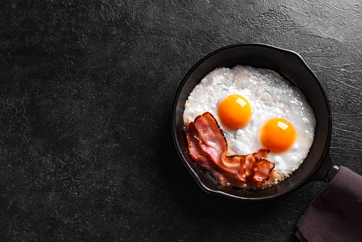 Fried eggs and bacon for breakfast on black background, top view, copy space. Homemade traditional keto breakfast. Good morning concept.