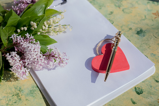 Mock up letter with a love box in the shape of a heart lies on a wooden white table with gypsophila flowers, a greeting card for Valentine's Day with a place for your text. Flat lay, top view photo.