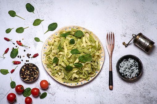 Homemade Italian traditional pasta Tagliatelle with pesto sauce and fresh basil leaves in a ceramic bowl on a rustic wooden background. Top view.