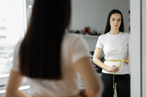 Woman looking the mirror measuring her waist