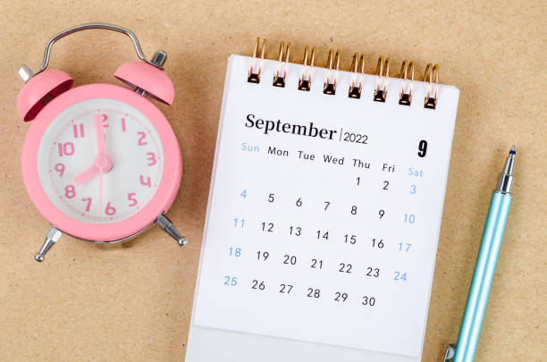 istock September 2022 Desk calendar with pink alarm clock on brown background. 1393277786