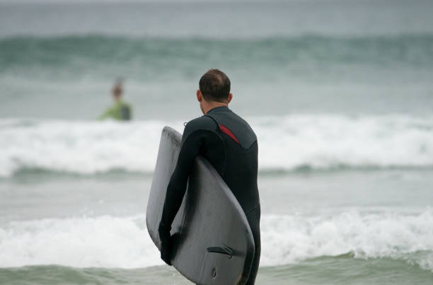 istock Young man entering the water before surfing off the Cornish Coast 1393280294