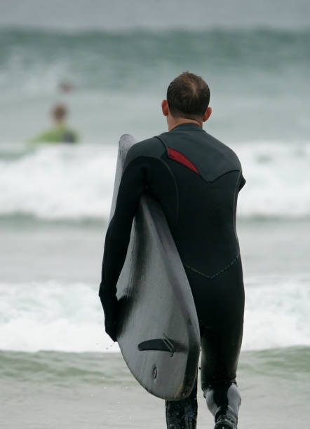 istock Young man entering the water before surfing off the Cornish Coast 1393281783