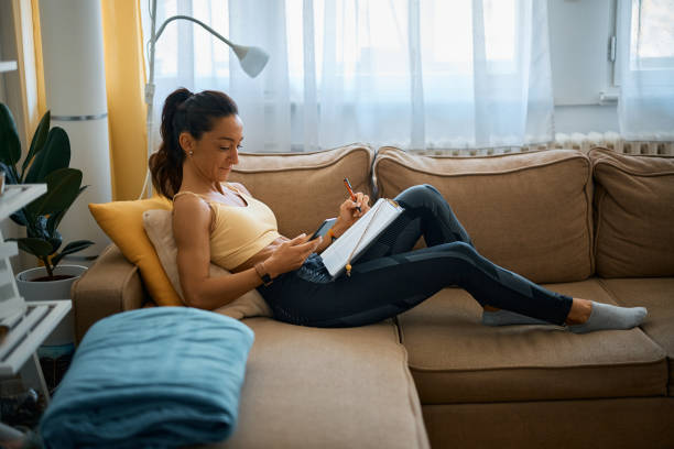 istock Athletic woman using cell phone and taking notes while relaxing on the sofa at home. 1393281969