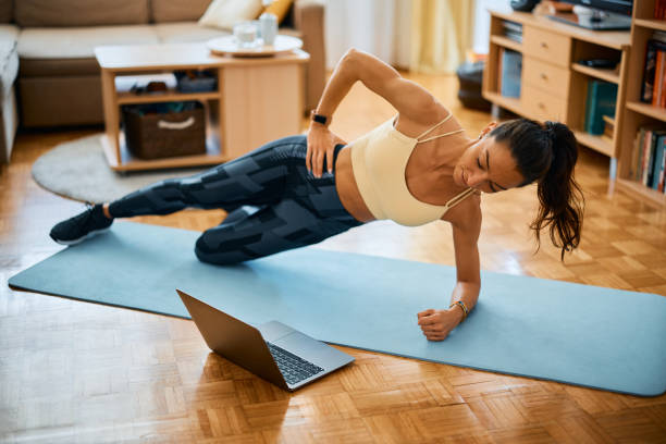istock Female athlete in side plank pose following online exercise class over laptop at home. 1393283821