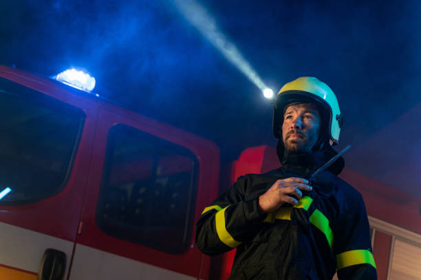 istock Low angle view of firefighter with fire truck in background at night. 1393283990