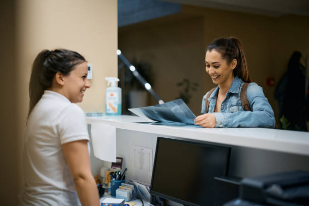 Happy woman looking at her X-ray image at reception desk of physical therapy center. Happy patient examining her X-ray scan at physical therapy reception desk. sports training clinic stock pictures, royalty-free photos & images