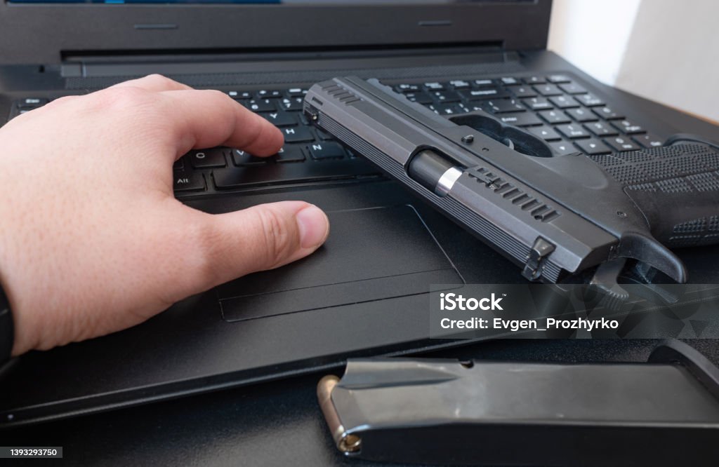 Criminal with handgun placed on a laptop computer. Cyber war, data security, terrorism threat. Concept image. Computer Stock Photo