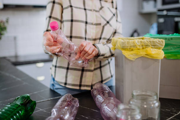 istock Midsection of woman throwing empty plastic bottle in recycling bin in kitchen. 1393307225