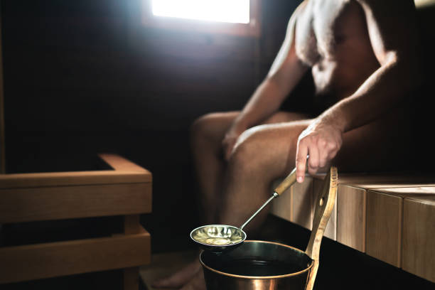 uomo in sauna. bagno turco finlandese. persona che versa acqua sulle pietre calde dal secchio. relax tradizionale e benessere in finlandia. - throwing people stone tossing foto e immagini stock