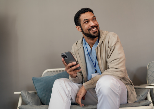 A happy young male doctor or caregiver with smartphone relaxing.