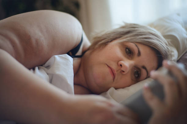 落ち込んだ孤独な太った女性は、自宅でベッドに横たわって考えています。 - mature adult sadness overweight women ストックフォトと画像