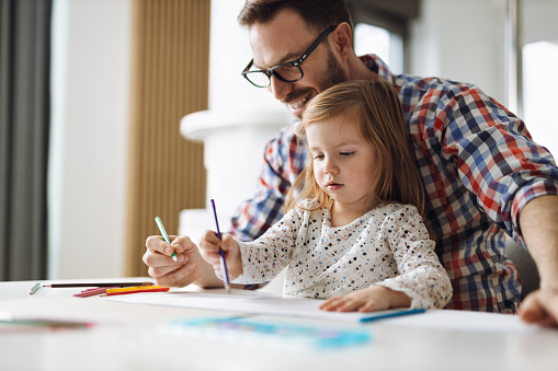 Little girl and her father having fun while coloring in the living room