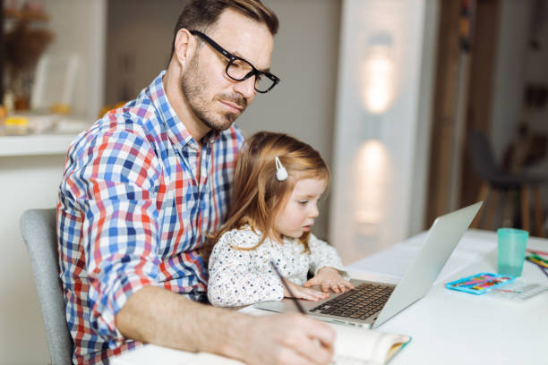 istock Young father using laptop while his daughter sitting on his lap at home 1393342059